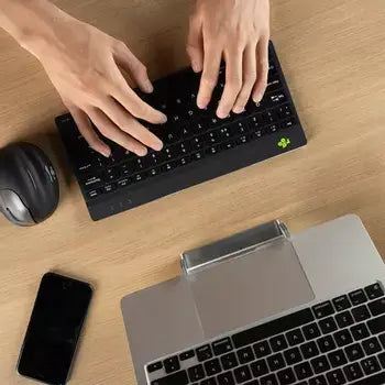 Compact Ergo-R Black mini keyboard with hands typing, placed beside a laptop and mouse on a desk.