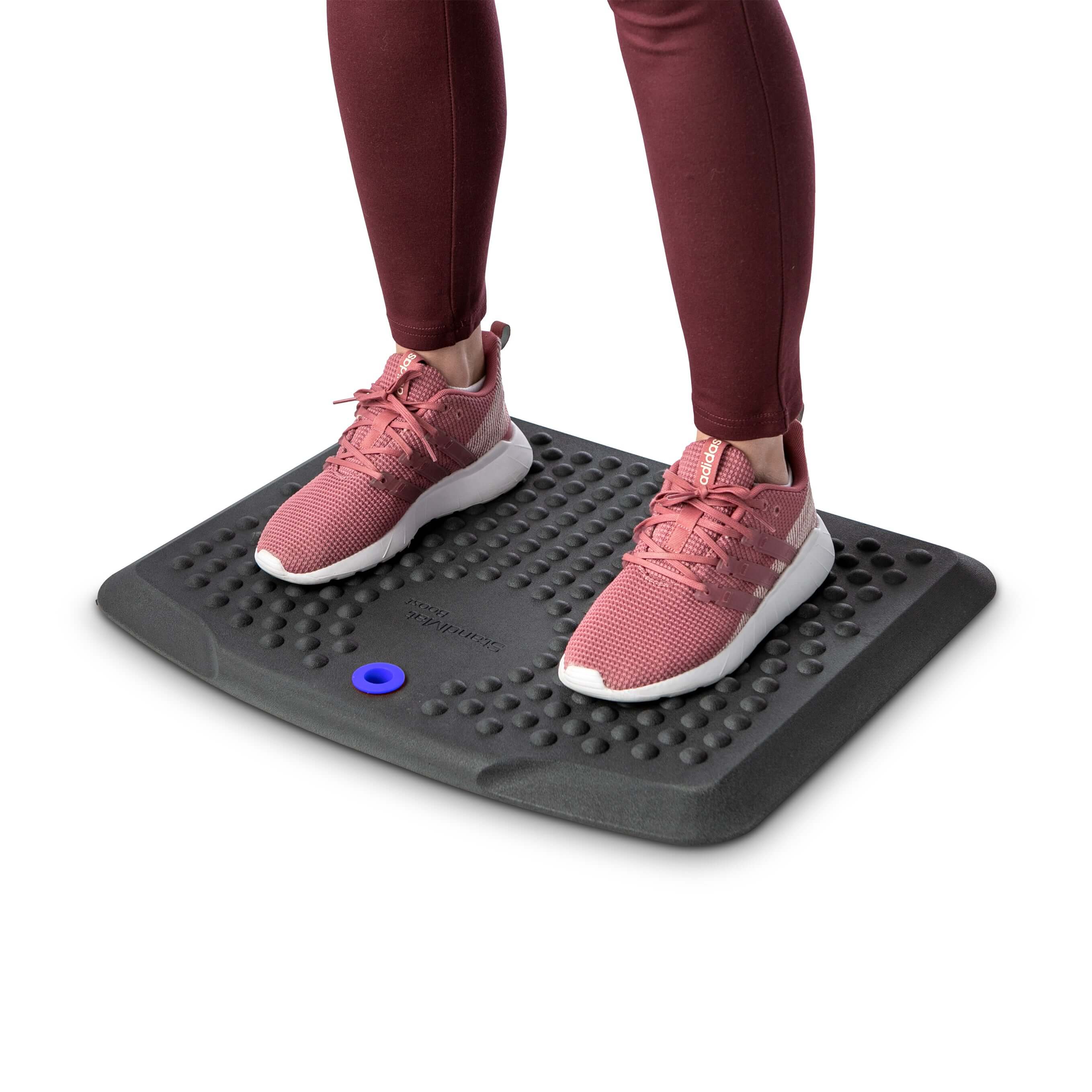 Person standing on black StandMat Boost ergonomic workstation mat with bubble pattern for improved comfort and blood circulation.