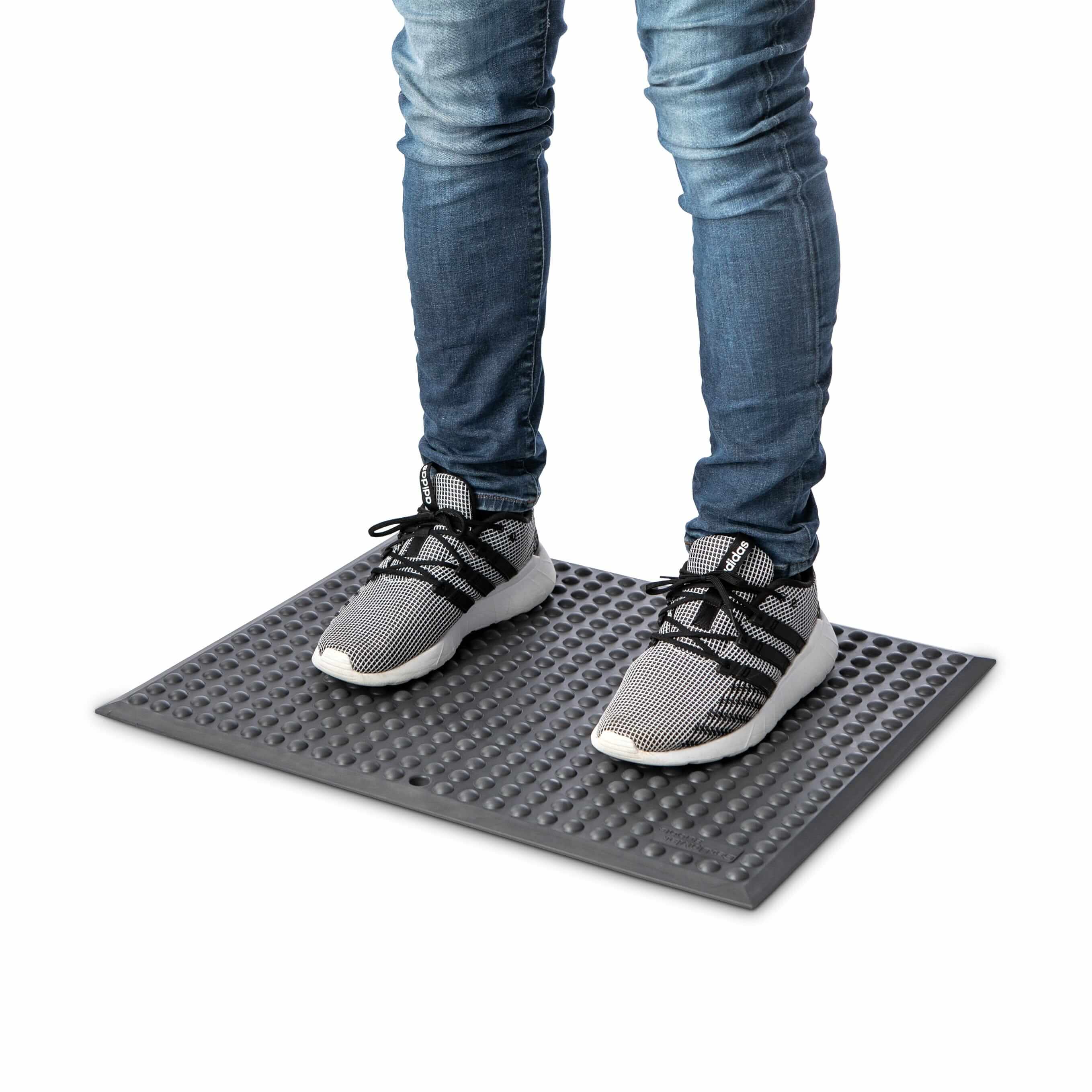 Person standing on GetUpMat Bubble workstation mat, dark grey, designed to reduce fatigue and improve circulation during standing tasks.