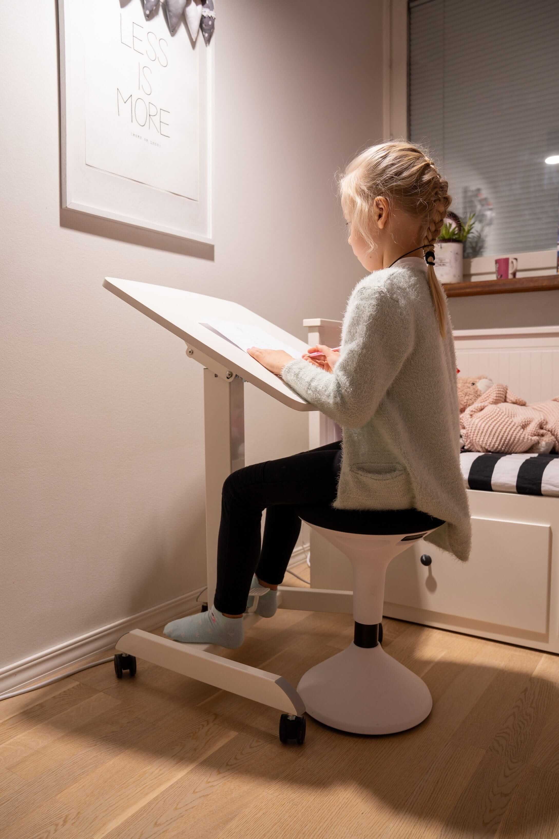 Child using the GetUpDesk Tilt adjustable desk with stopper in a cozy room setting.