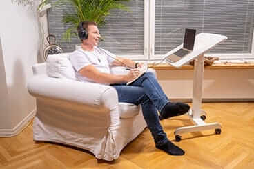 Man using GetUpDesk Tilt adjustable desk with laptop in living room.