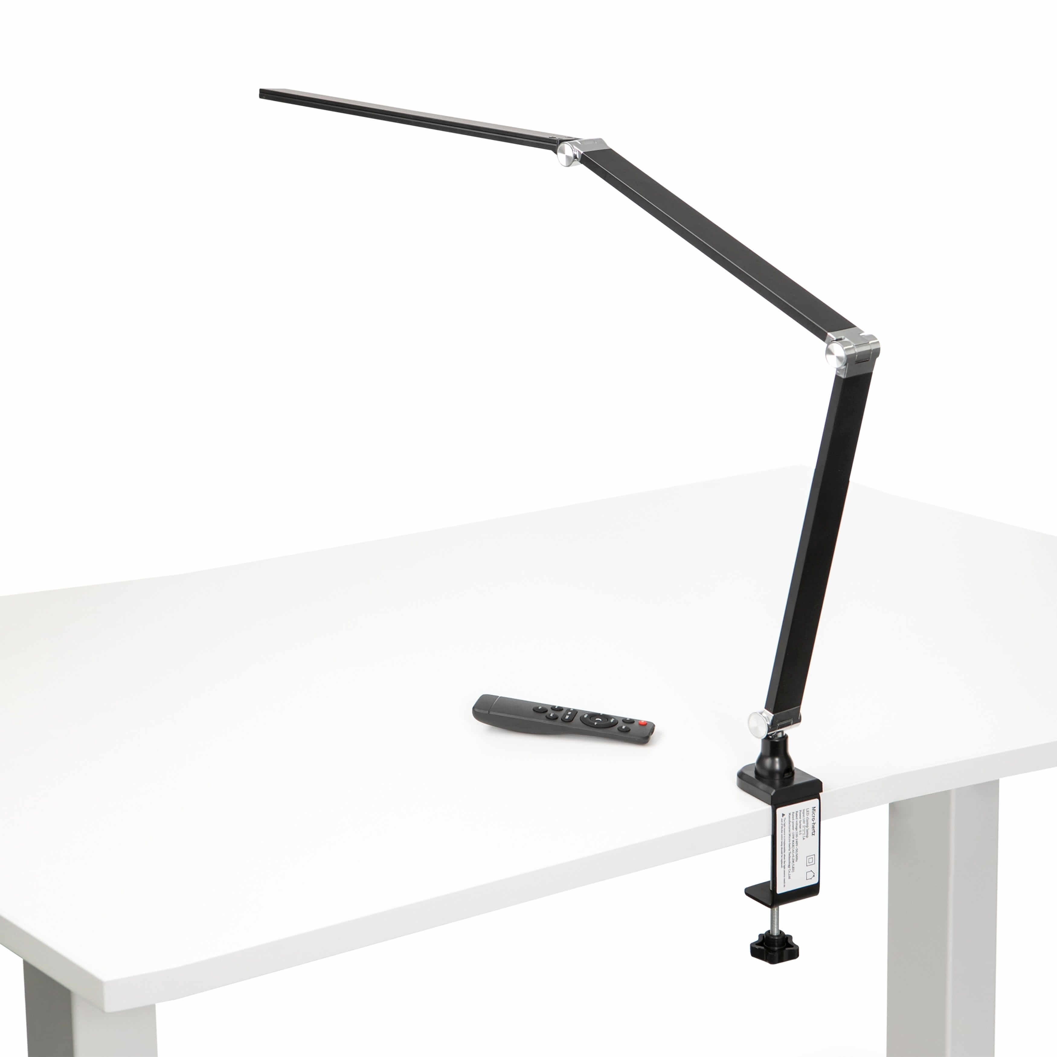 Black LED desk lamp with long metal arm and aluminium joints on white desk, featuring a remote control, ideal for modern workspaces.