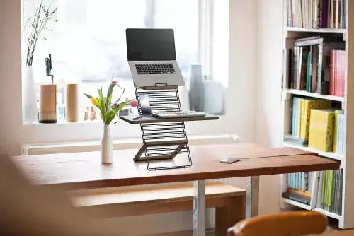 Light grey Standfriend ergonomic stand on desk with laptop, promoting health and efficiency by allowing standing work positions.