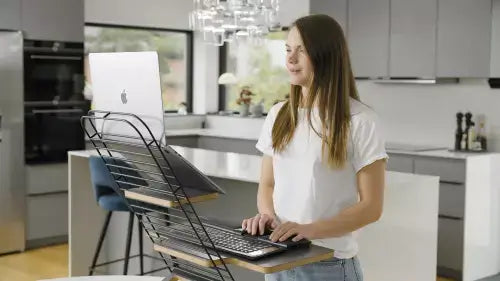 Woman using Standfriend ergonomic stand while working on laptop in modern kitchen.