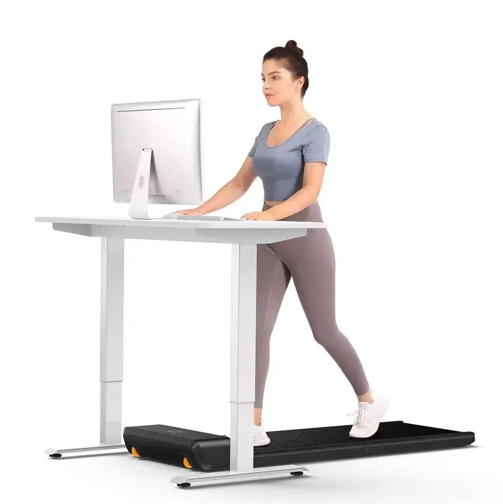 Woman using WalkingPad Pro under desk treadmill for office exercise at standing desk.