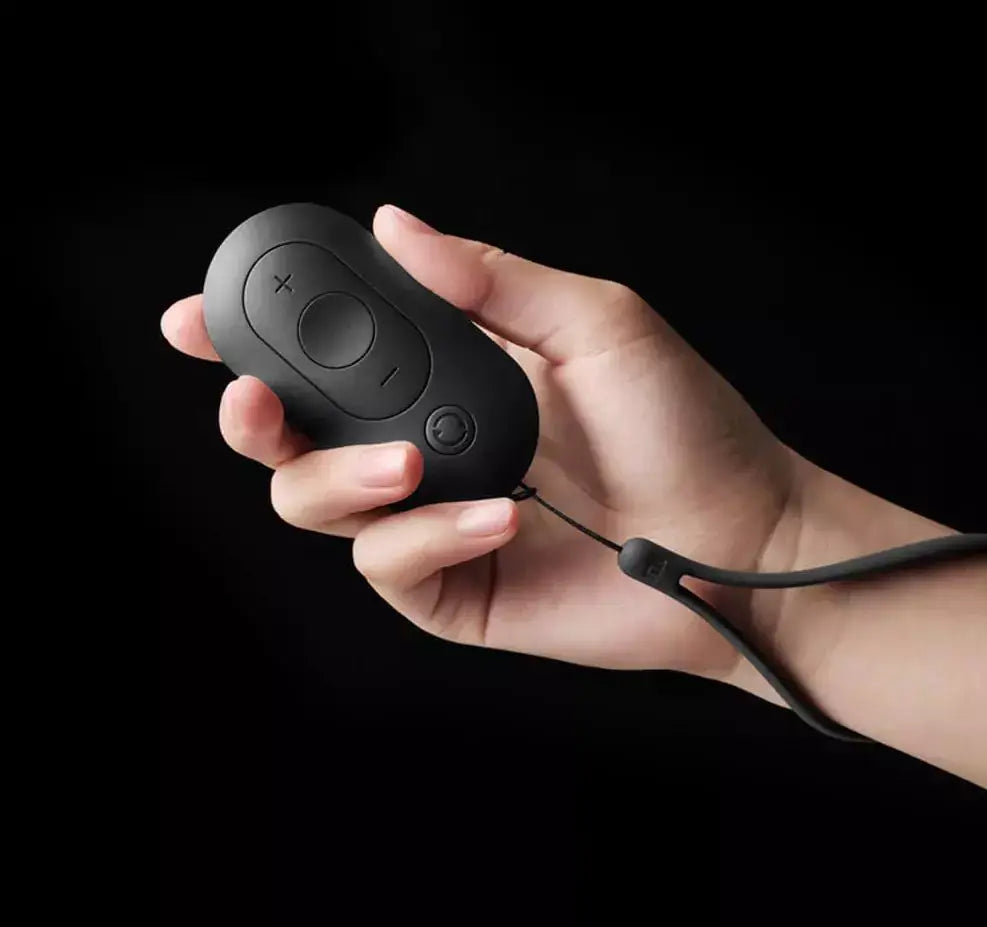 Hand holding a black remote control with wrist strap against a dark background.