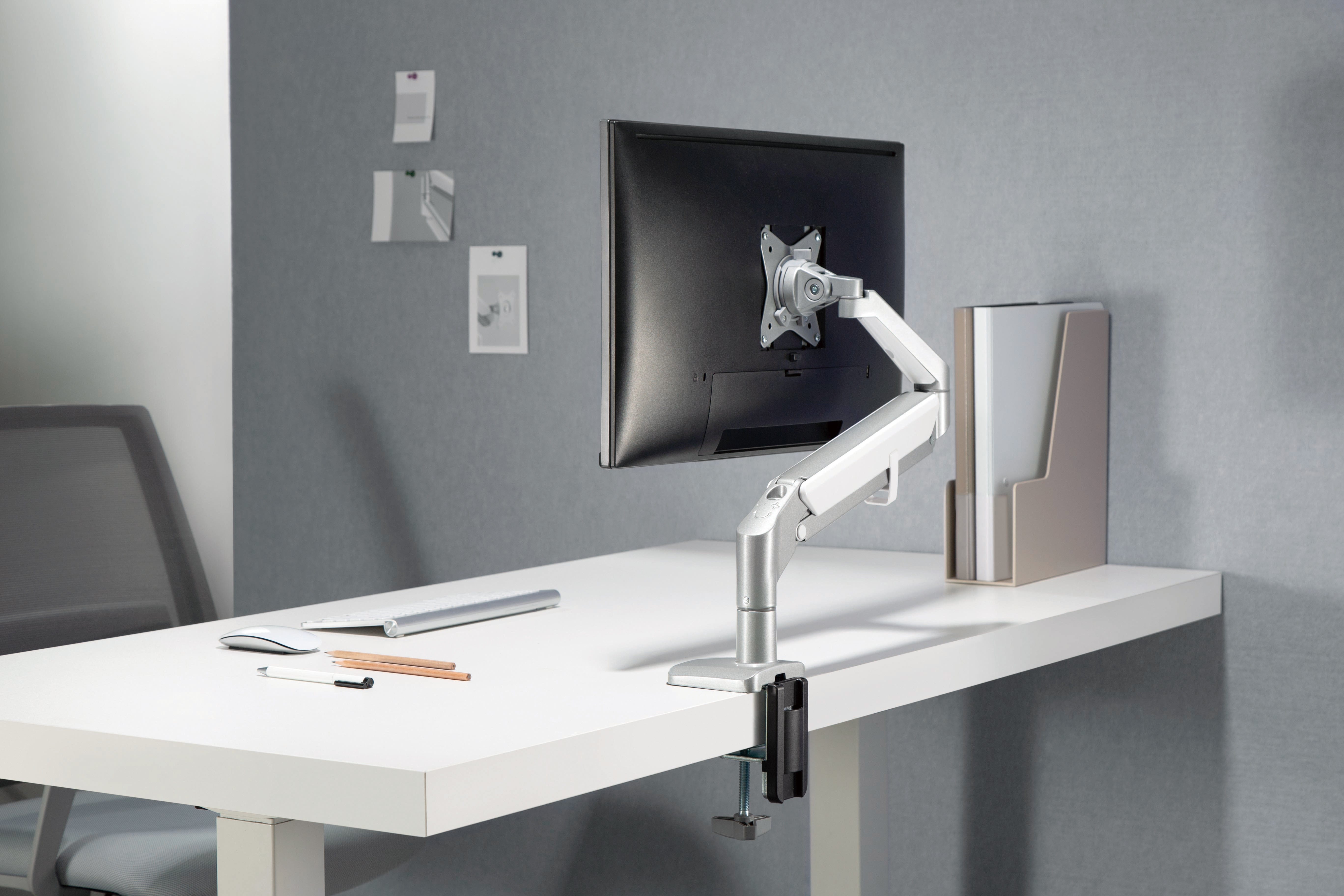 Silver LCD monitor arm with gas spring on a white desk, showcasing ergonomic workspace setup by ErgoFinland.