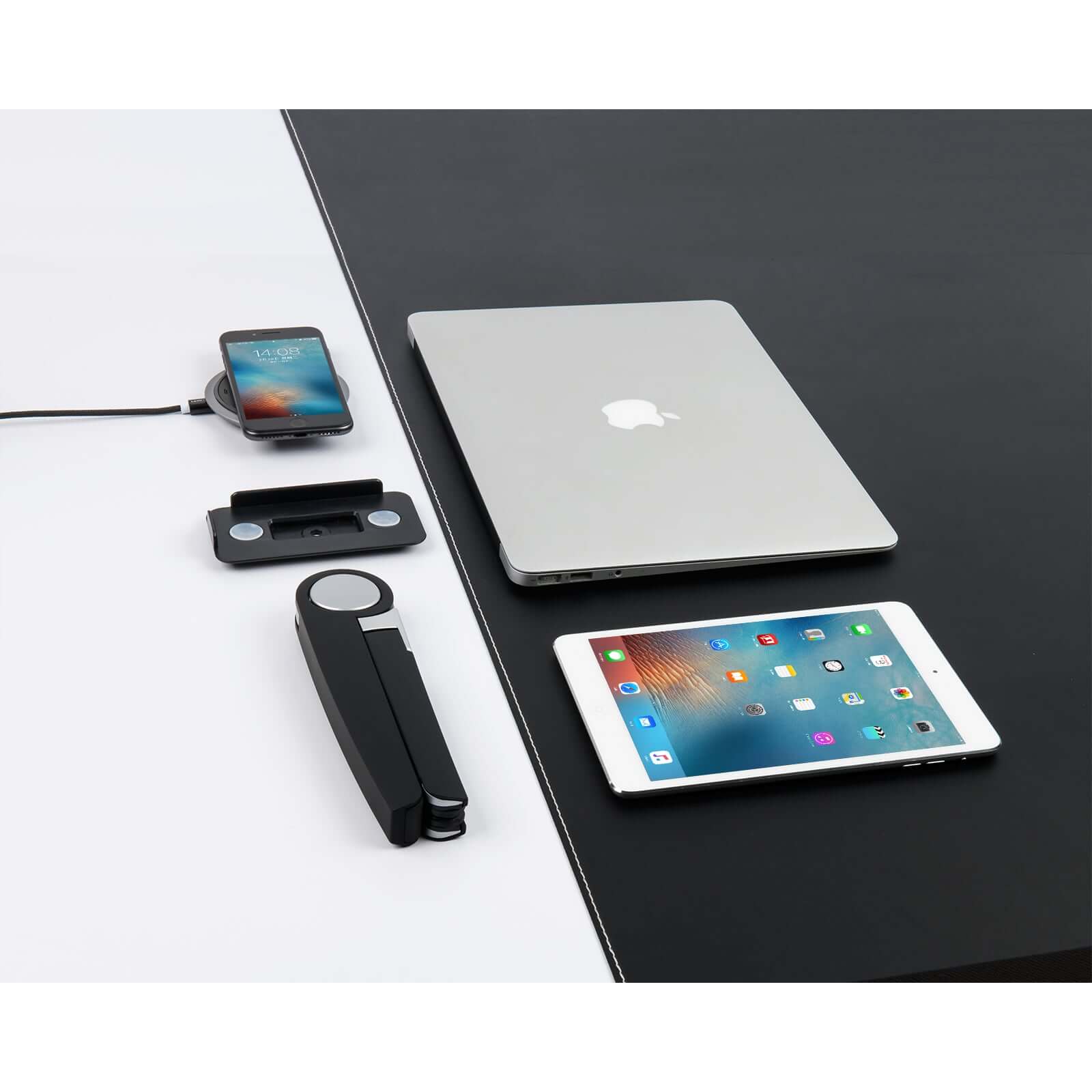 Black Spider laptop and tablet stand next to a laptop, tablet, smartphone, and charging device on a two-tone desk surface.