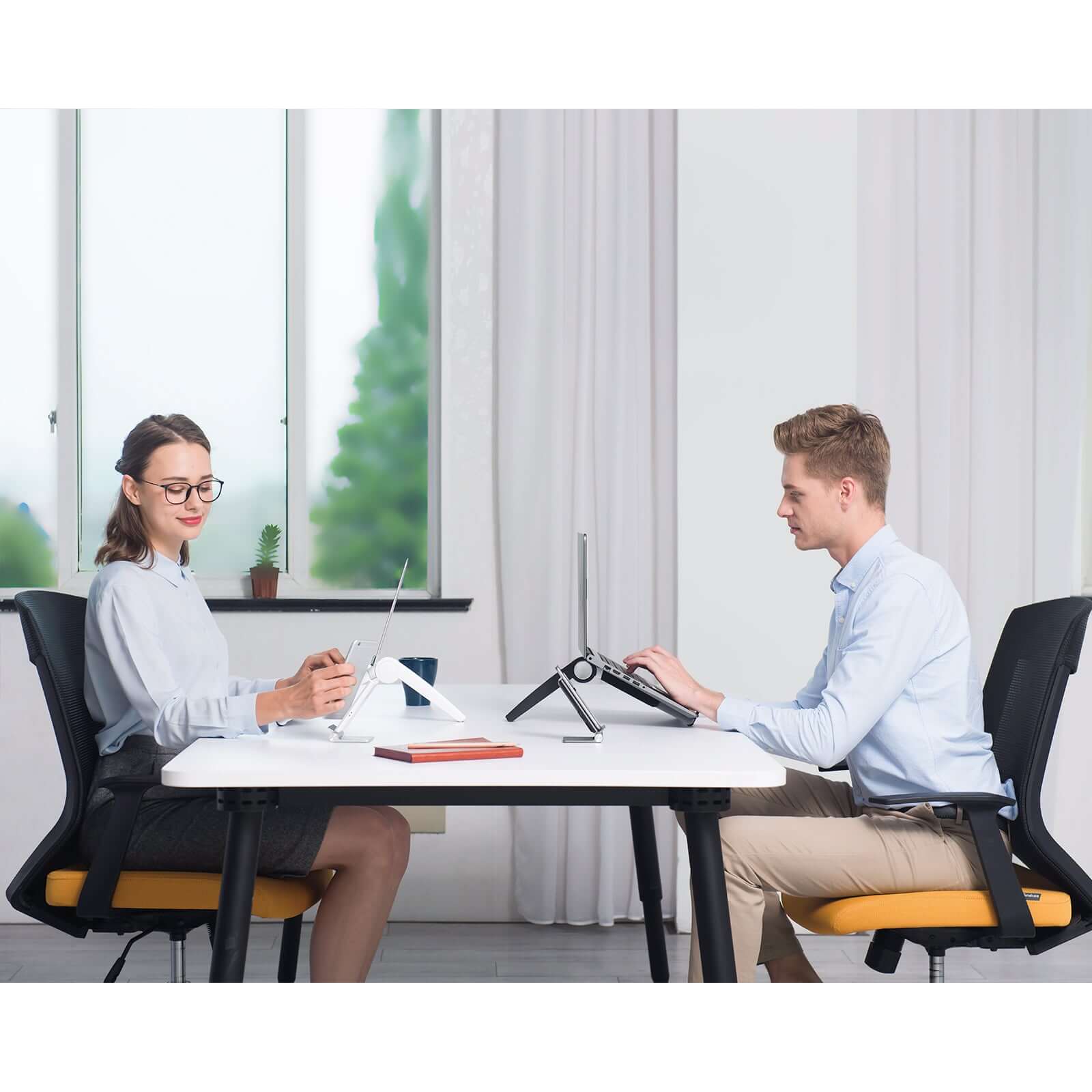 Two people using laptop and tablet stands at a modern office desk, enhancing workspace with sleek and ergonomic designs.