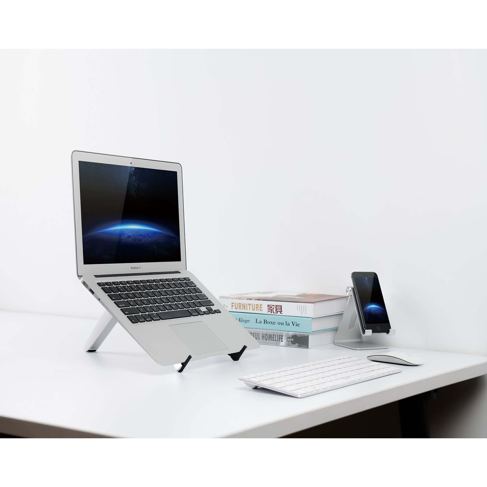 White Spider laptop and tablet stand on desk with laptop, phone, keyboard, and books, showcasing modern workspace setup.